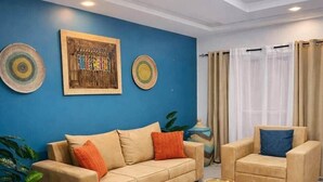 Un salon avec un mur bleu, deux canapés, une table basse et un grand vase.