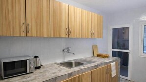 Une cuisine moderne avec des meubles en bois, un four à micro-ondes encastré, un évier et une fenêtre donnant sur un balcon.