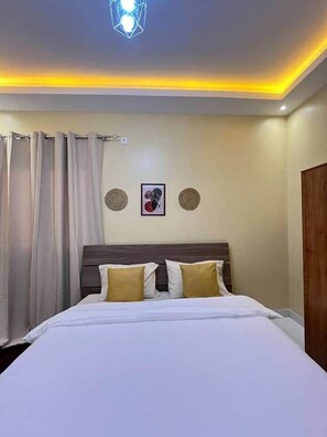 Una habitación de hotel con una cama, cortinas, cabecero y lámpara en el techo.