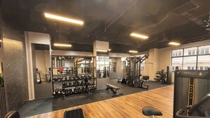 Een sportschool met diverse fitnessapparaten, een houten vloer en grote ramen.