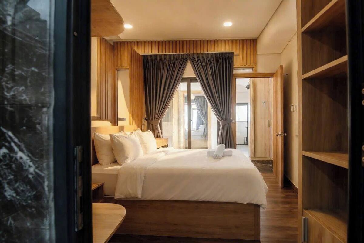 A hotel room with a bed, bedside tables, a wardrobe, and a large window with curtains.