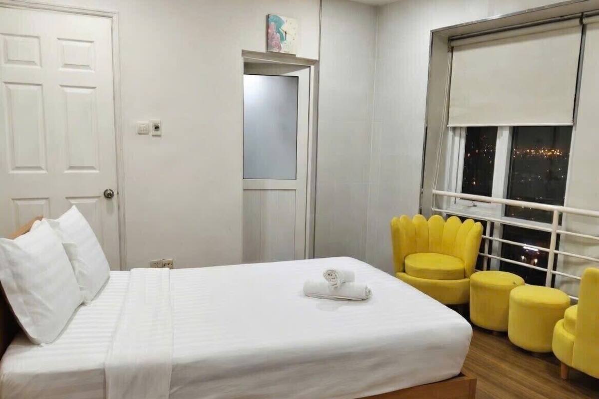 A hotel room with a bed, a window with a view of the night sky, a door, and a small shelf with a picture.