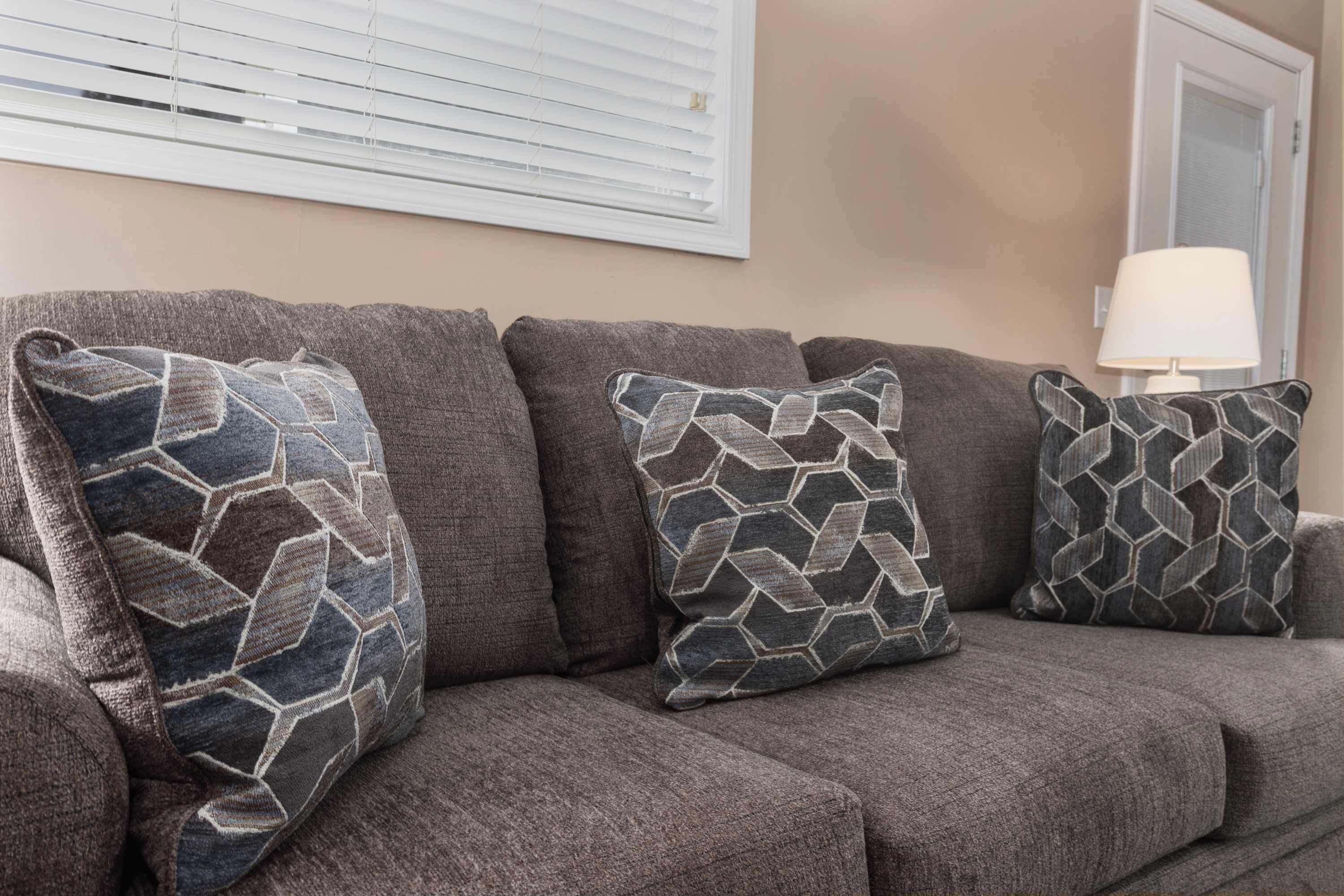 A grey sofa with patterned cushions and a lamp on a table.