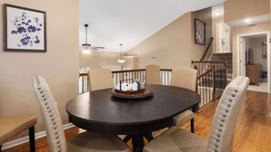A dining area with a round table, beige upholstered chairs, and a chandelier.