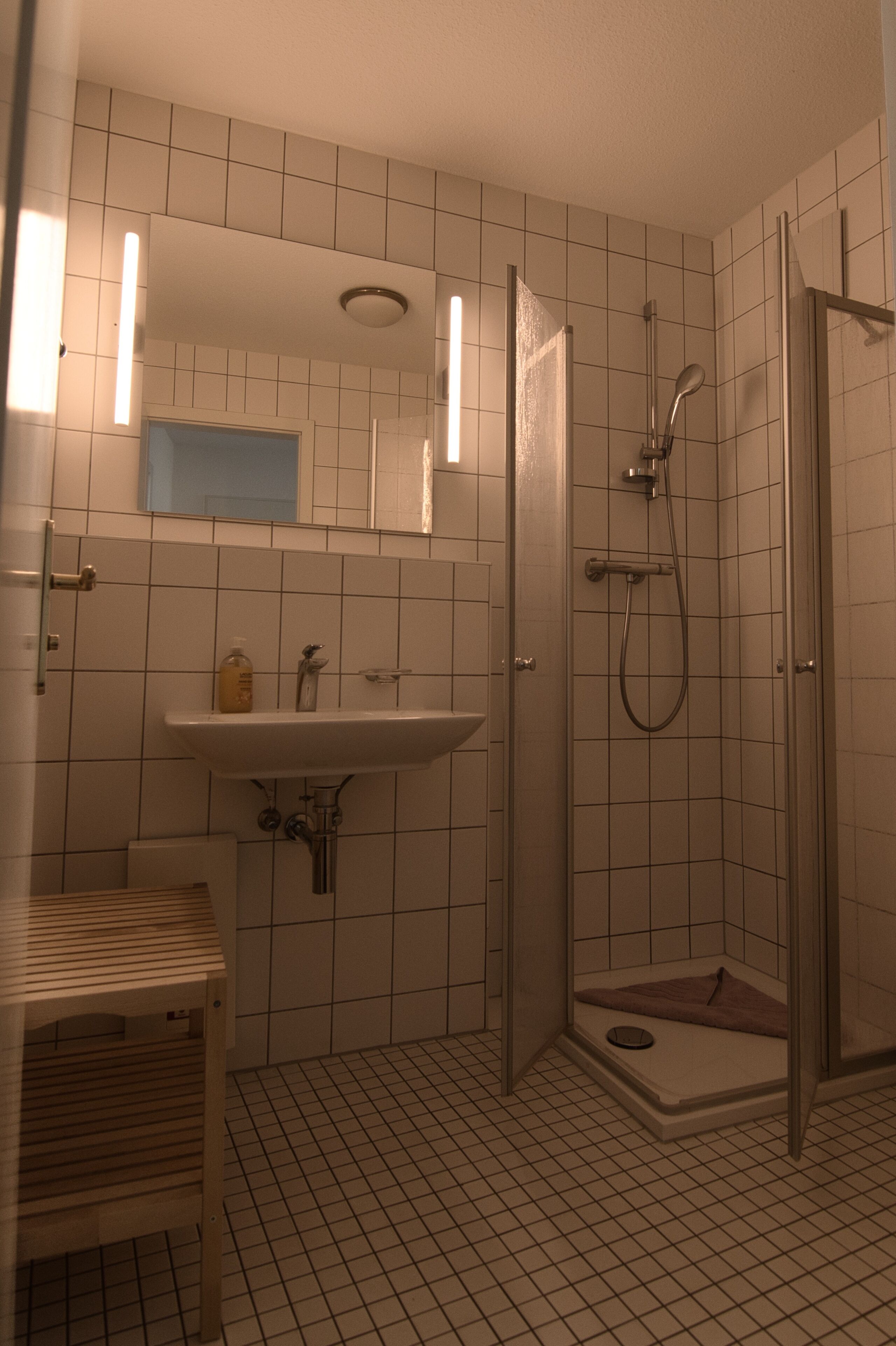 Une salle de bain avec un lavabo, un miroir, une douche et un sol carrelé.
