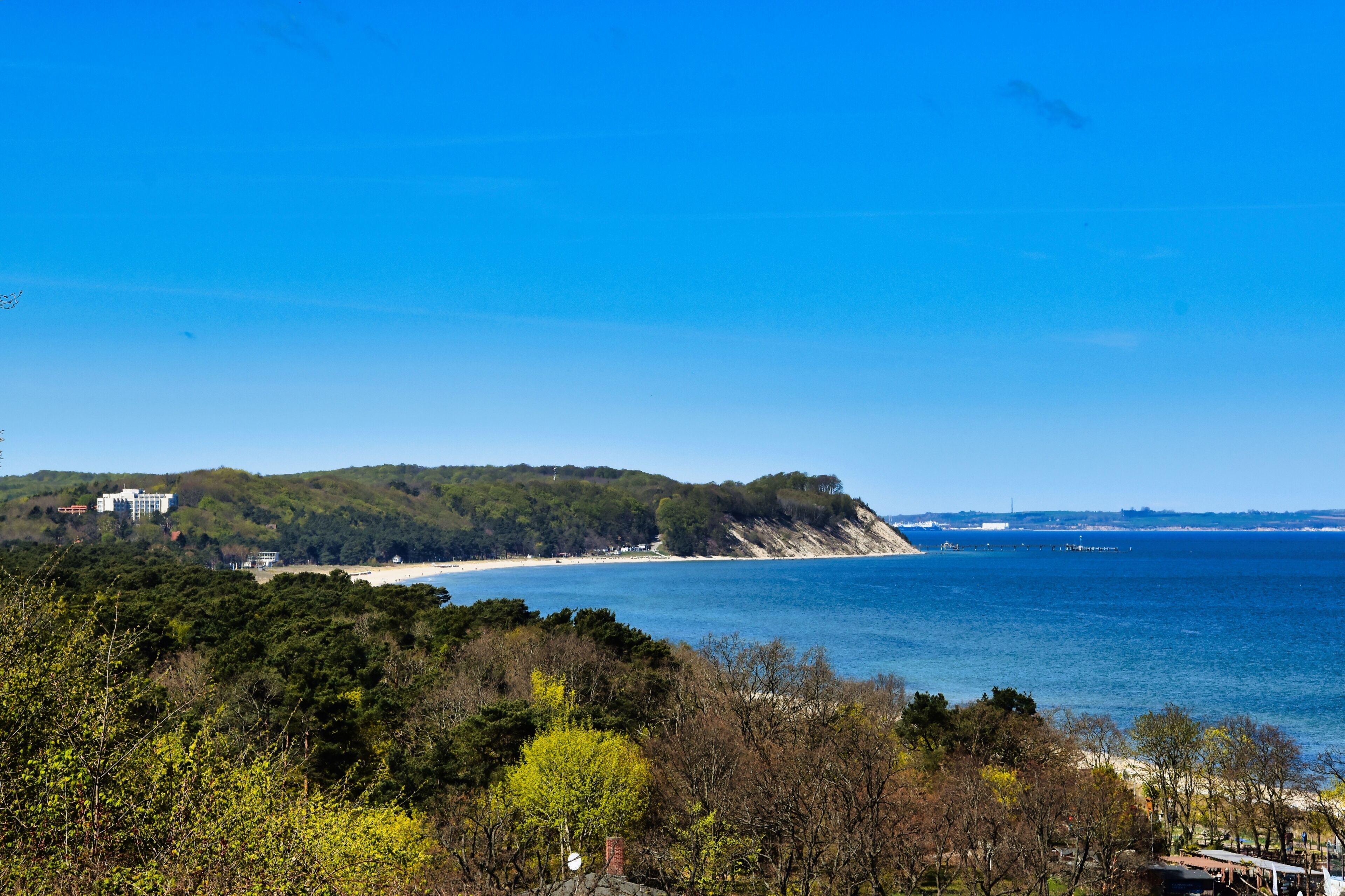 Un paysage côtier avec une plage, des collines boisées et un ciel bleu dégagé.