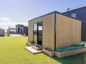 Una estructura moderna de madera con puerta de cristal, un pequeño jardín con escalones y una antena parabólica en el tejado.