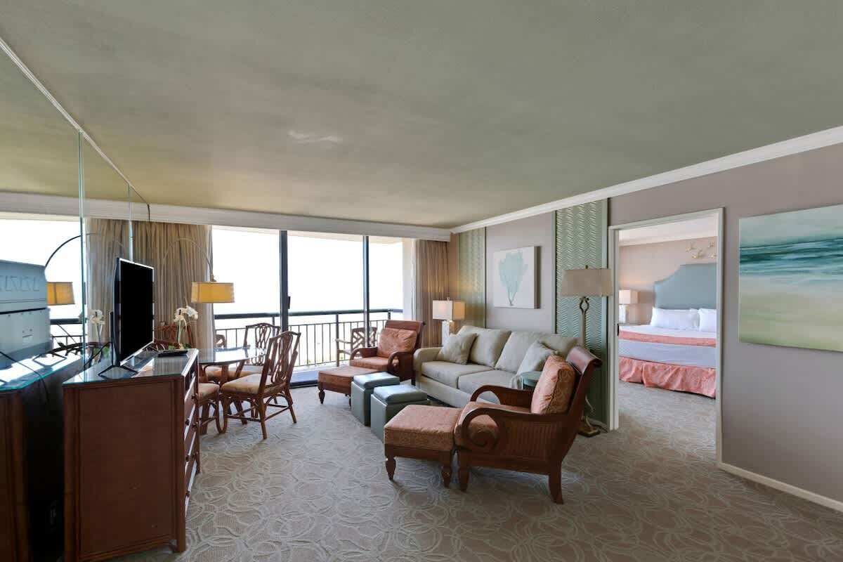 Habitación de hotel con una cama grande, un sofá, un escritorio y un televisor. Tiene un balcón con vistas a la ciudad.