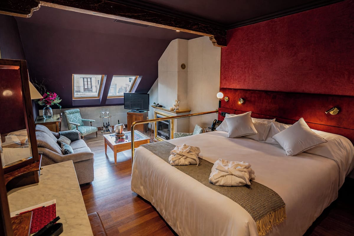 Une chambre d’hôtel dotée d’un grand lit, d’un coin salon avec un canapé et des fauteuils, d’une petite table avec une lampe et d’un téléviseur.