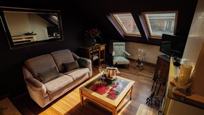 Un salon confortable avec un canapé, une table basse en verre et un téléviseur. Deux fenêtres laissent entrer la lumière naturelle.