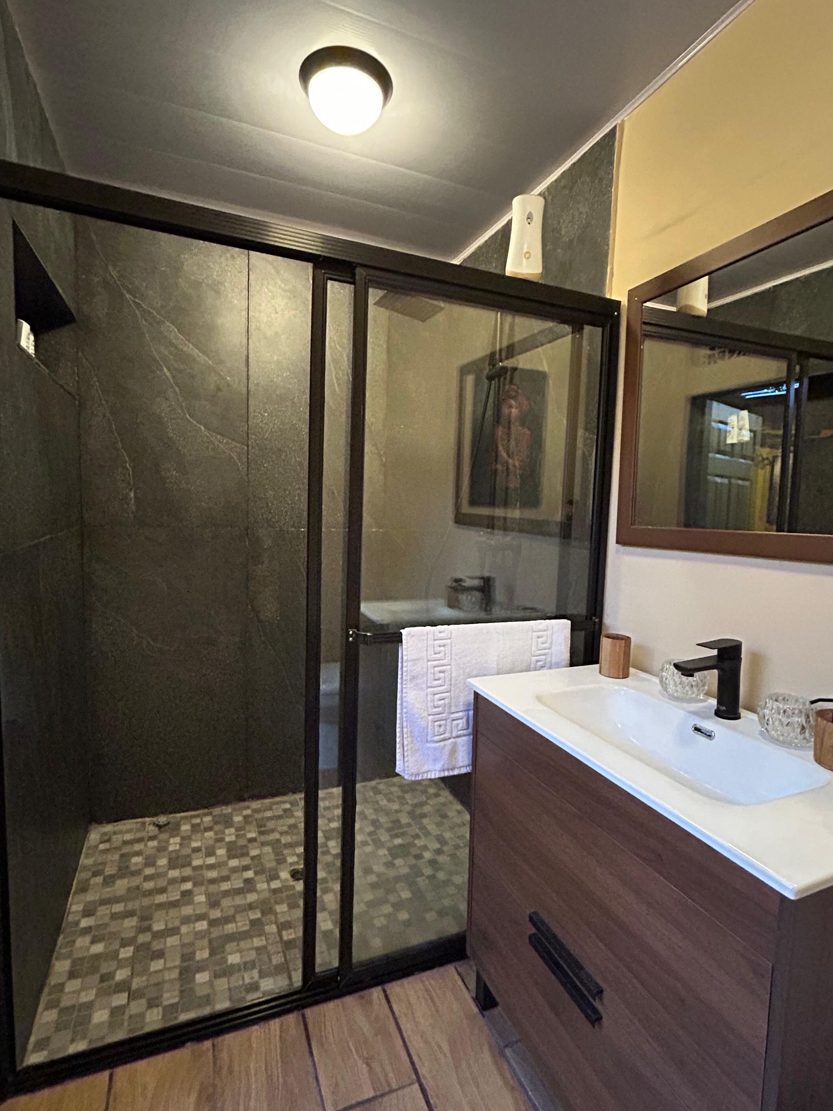 A bathroom with a glass-enclosed shower, a white sink, a wooden vanity, and a mirror.