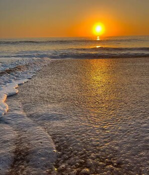 En strand där solen går ner över havet och skapar en skimrande stig på den våta sanden.