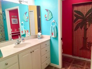 Baño con pared turquesa, lavamanos blanco y espejo. Hay un perchero con una toalla colgada.