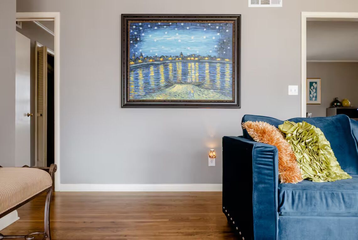 Une pièce avec un canapé bleu foncé, une œuvre d’art encadrée représentant une scène nocturne et une petite table avec une lampe.