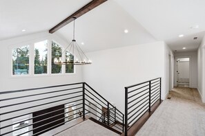 Amplia habitación con techo alto, ventanas grandes, chimenea y escalera con barandilla metálica.