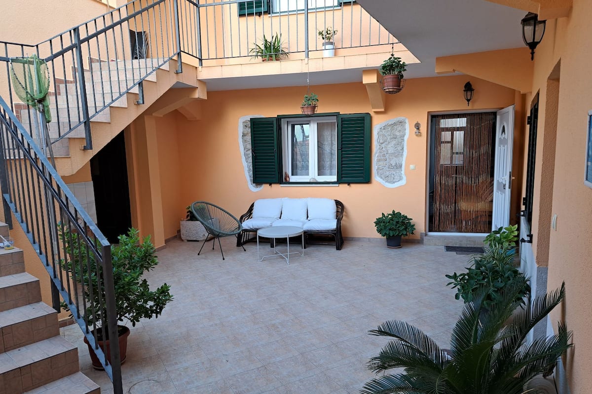 Un cortile con un divano bianco, una poltrona in vimini e piante in vaso.