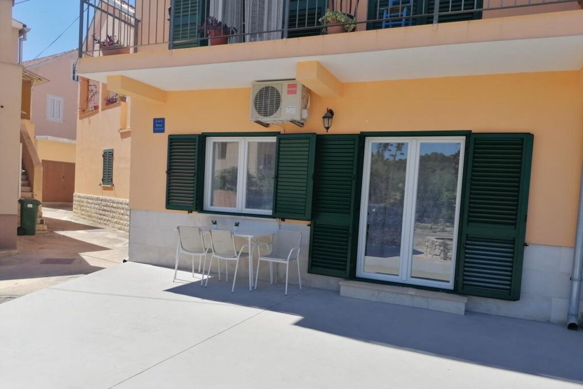 Un edificio con balcón, una mesa con sillas y una ventana con persianas.