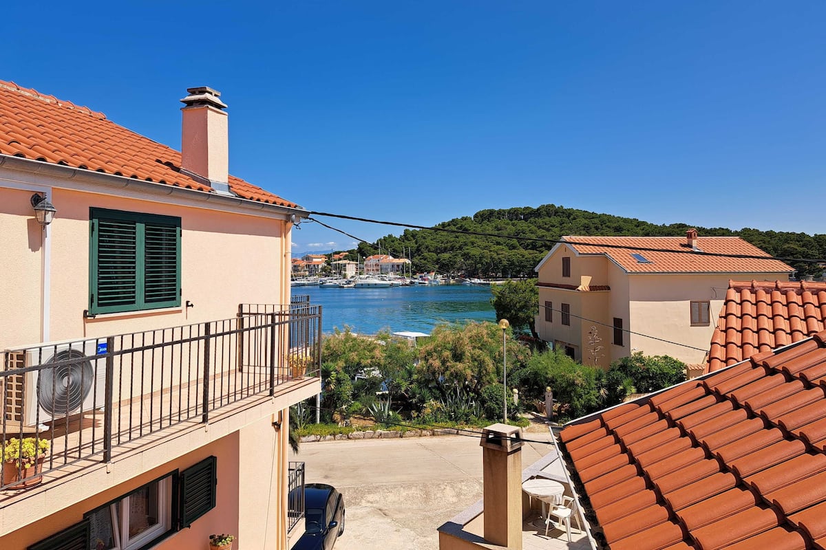 Una zona residenziale costiera con tetti in tegole di terracotta, un cielo azzurro limpido e un porto turistico sullo sfondo.