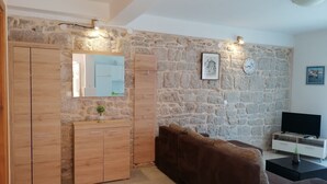 A living room with a stone wall, wooden wardrobe, and a brown sofa. - Sea View Apartments Kukljica (Kukljica)