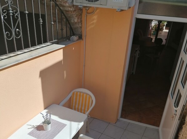 Un piccolo spazio esterno con un tavolo, una sedia, una pianta in vaso e una porta che dà su un ambiente interno.
