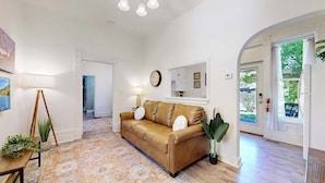 A spacious living room with a brown leather sofa, a patterned rug, and a large window with a view of greenery.