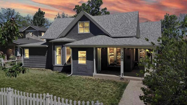 A two-story house with a dark exterior, a covered porch, and a well-maintained lawn.