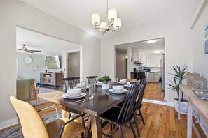 Un comedor con una mesa de madera dispuesta para cuatro personas, rodeada de sillas negras. Hay una araña sobre la mesa, y una planta colocada en ella.