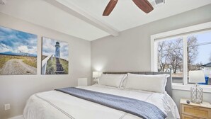 Un dormitorio con una cama grande, una mesita de noche, una ventana con vistas y dos cuadros colgados en la pared.
