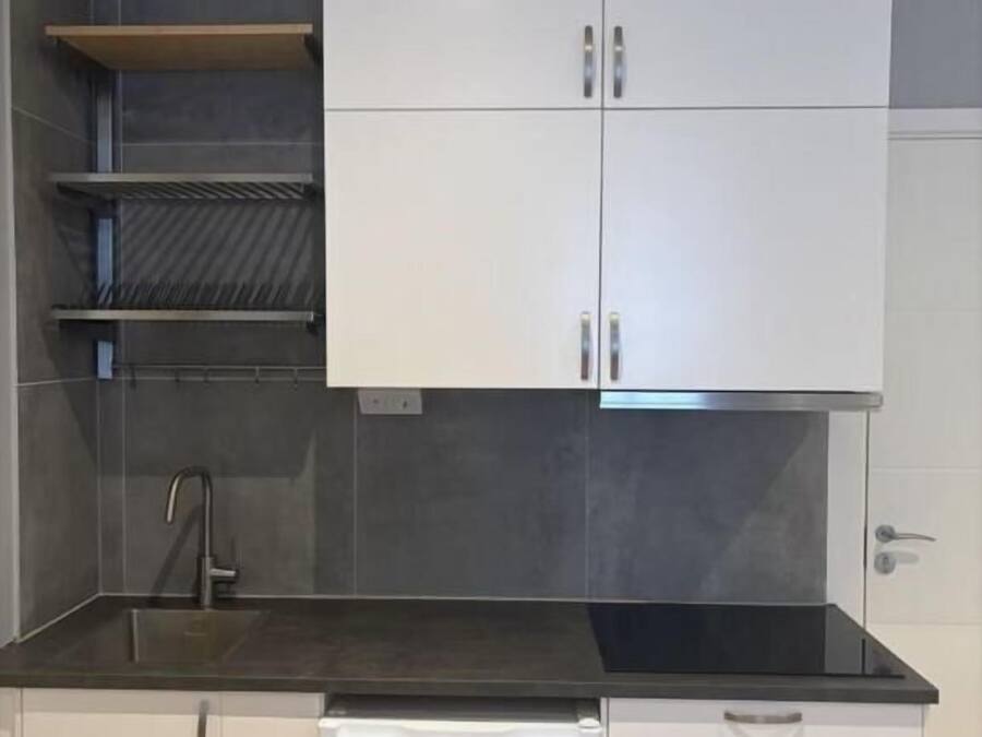 Cozinha compacta com armários brancos, bancada preta e pia de aço inoxidável.