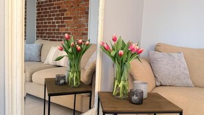 A living room with a sofa, two small tables with vases of flowers, and a mirror reflecting the room. - Villa Bäckagård Bed & Breakfast (Åstorp)