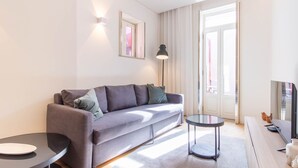 Ein modernes Wohnzimmer mit einem grauen Sofa, einem kleinen runden Tisch, einer Stehlampe und einem Fernseher.