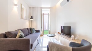 Ein modernes Wohnzimmer mit einem grauen Sofa, einem runden Couchtisch und einem Flachbildfernseher auf einer Holzkommode.