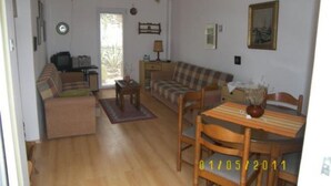 A living room with a sofa, a dining table, and a TV. There is a window and a door leading outside. - Apartments Zlatko (Vodice)