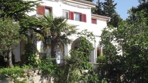 A white building with red shutters, surrounded by greenery and trees. - Apartments Zlatko (Vodice)