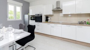 A modern kitchen with white cabinets, a black oven, a microwave, and a coffee maker. - Apartments and Room Ljubica i Branko (Lopar)