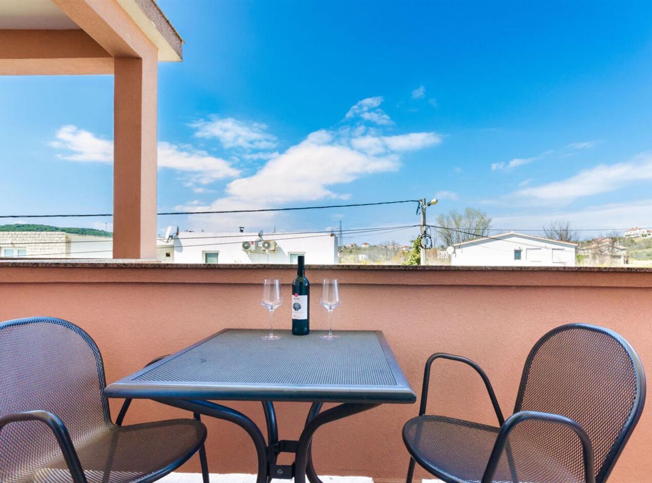 Un balcone con tavolo e sedie, una bottiglia di vino e bicchieri da vino.