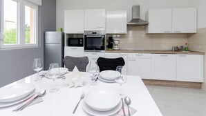 A modern kitchen with white cabinets, a built-in oven, microwave, and coffee maker. - Apartments and Room Ljubica i Branko (Lopar)
