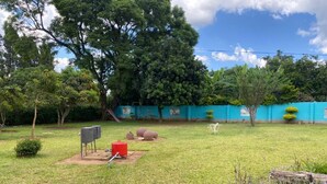 A grassy outdoor area with a blue fence, trees, and a red object on the ground.