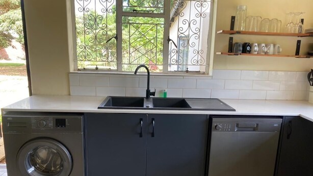 A compact kitchen with a washing machine, dishwasher, and a window with a metal grill.