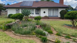 A house with a solar panel roof, a garden with various plants, and a well-maintained lawn.