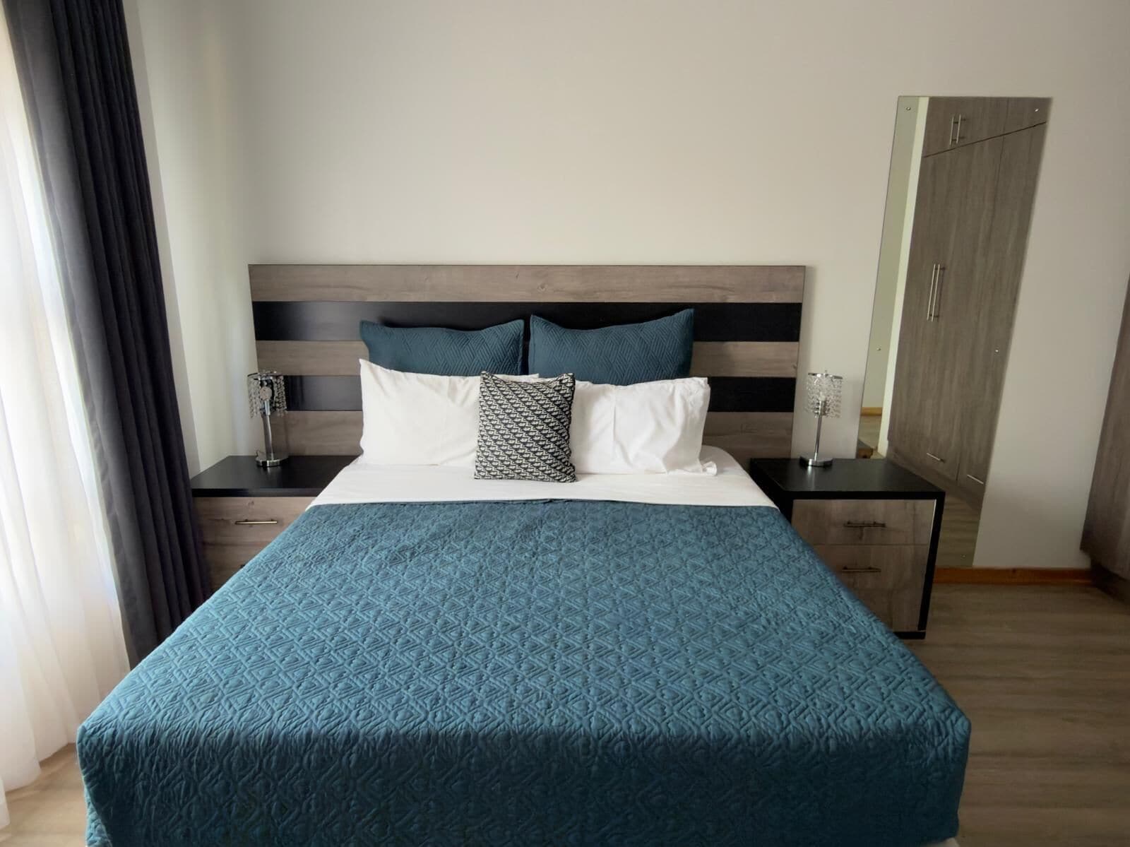 Een netjes opgemaakt bed met een geborreld sprei, twee nachtkastjes met lampen, een houten hoofdbord en een kledingkast.