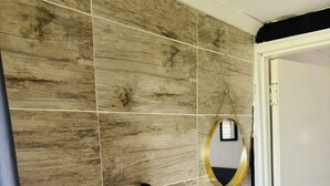 A bathroom with a wooden wall, a black towel rack, a white sink, and a gold-framed mirror.