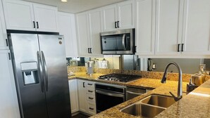 A modern kitchen with stainless steel appliances, granite countertops, and white cabinetry. - Modern & Spacious 1 br + bonus rm 2 bthrm apartment in Marina District high rise (San Diego)