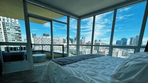 A modern hotel room with a large bed, a seating area, and a panoramic city view through floor-to-ceiling windows. - Modern & Spacious 1 br + bonus rm 2 bthrm apartment in Marina District high rise (San Diego)