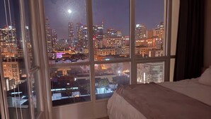 A bedroom with a large window offering a city view at night. - Modern & Spacious 1 br + bonus rm 2 bthrm apartment in Marina District high rise (San Diego)