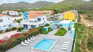 A resort with a swimming pool, white lounge chairs, and colorful buildings.