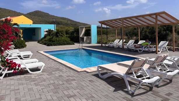 A swimming pool with lounge chairs, a covered area, and a building in the background.