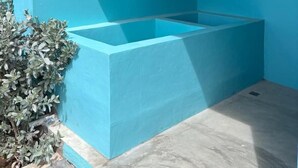 A blue-tinted room with a bathtub, a small shelf, and a security camera.