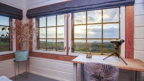 A room with a desk, a chair, a telescope, and a view of the countryside through large windows. - The Wooden House, Breanish Uig, Isle of Lewis (Uig)