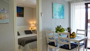 Ein Zimmer mit einem Bett, einem Nachttisch, einer Lampe sowie einem Essbereich mit Tisch, Stühlen und einer Obstschale.
